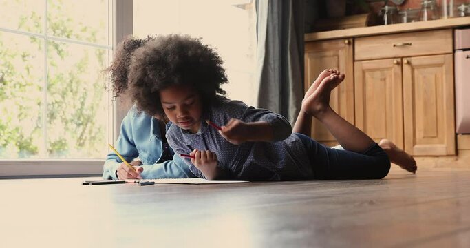 African family spend time at modern home, mother and little 6s daughter chatting while lying on warm wooden kitchen floor draw pictures in sketchbook enjoy hobby and talk. Pastime and leisure concept