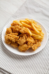 Homemade Fried Chicken Bites and French Fries on a plate, side view.