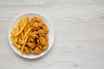 Homemade Fried Chicken Bites and French Fries on a plate on a white wooden table, overhead view. Flat lay, top view, from above. Copy space.