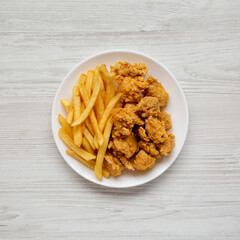 Homemade Fried Chicken Bites and French Fries on a plate on a white wooden background, overhead view. Flat lay, top view, from above.
