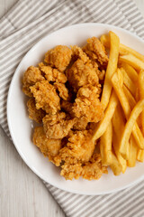 Homemade Fried Chicken Bites and French Fries on a plate on cloth, view from above. Flat lay, top view, overhead. Close-up.