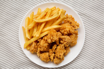 Homemade Fried Chicken Bites and French Fries on a plate on cloth, overhead view. Flat lay, top view, from above. Close-up.