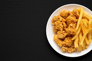 Homemade Fried Chicken Bites and French Fries on a plate on a black surface, overhead view. Flat lay, top view, from above. Copy space.