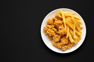 Homemade Fried Chicken Bites and French Fries on a plate on a black background, overhead view. Flat lay, top view, from above. Copy space.
