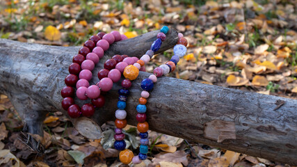Bright colorful ceramic and wooden handicraft beads lie on a fallen tree in the autumn forest. Traditional old Slavic culture.
