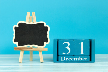 wooden calendar with the date of December 31 and an easel on a blue background, place for text