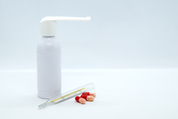 Compact Throat Spray, mercury thermometer and half transparent red capsules with dragees on white background. Concept: treatment of first signs of cold, seasonal viral diseases, flu. Space for text
