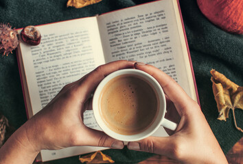 Top shot of female hands holding a cup of coffee over an open book