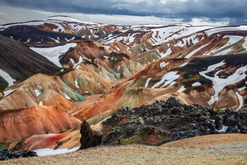 Amazing Icelandic landscape of colorful rainbow volcanic Landmannalaugar mountains, at famous Laugavegur hiking trail with dramatic snowy sky, and red volcano soil in Iceland