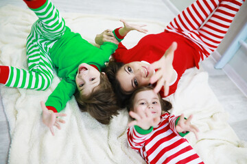 A family in striped pajamas is resting at home. Little children dressed as elves are lying on the sofa. Happy family.