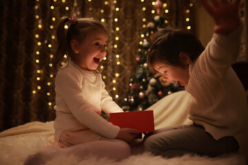 Family on Christmas eve at fireplace. Kids opening Xmas presents. Children under Christmas tree...