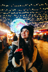 Close-up portrait of a happy girl in warm clothes walking around the evening Christmas market with...