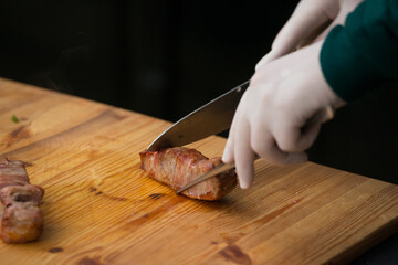 Closeup of chief cutting delicious roasted pork meat wrapped in bacon. Irish traditional dish wrapped pork loin with roasted garlic