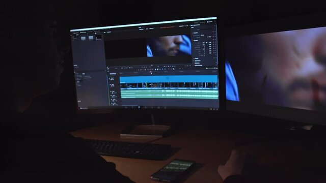 Young man editing a video clip on two monitors in studio. Dark night room.