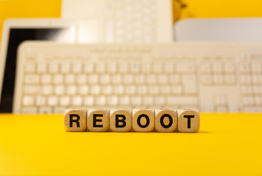 The word reboot written with real wooden dices in front of a yellow background with computers and keyboard