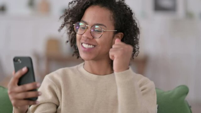 Portrait of Young African Woman Celebrating on Smartphone at Home 