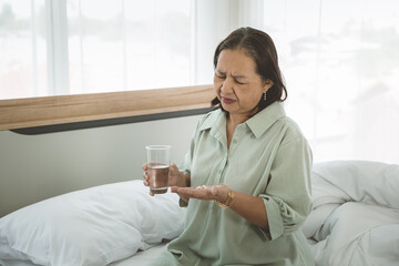 Depressed senior woman suffering from suicidal depression with some pills and glass of water.