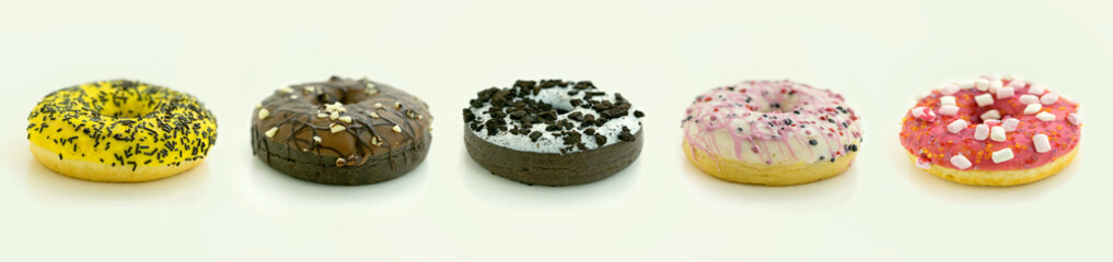 Banner size photo with multi colored different flavored glazed sprinkled donuts arranged in a row isolated on white background