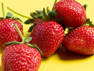 side view of juicy ripe strawberries lying on a bright yellow background. Healthy and delicious berries, vegetarian food, healthy food