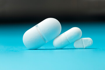 Three white  pills of different sizes on blue and black background, dosage