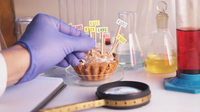 Healthy eating concept. The hand of the laboratory assistant is holding a magnifier in his hands, the cupcake on the table is decorated with tablets with the names of the additives of E. Food Laborato