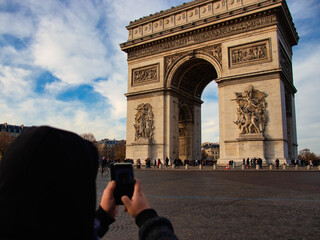 A tourist takes a photo of the Arc de Triomphe with his mobile phone