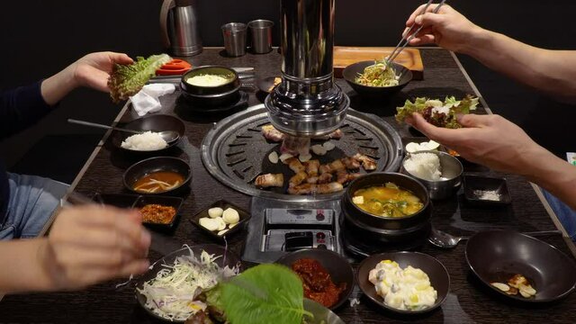 Couple Enjoying Korean Pork Belly Barbeque In A Restaurant - close up shot