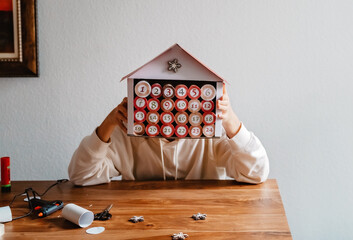 Teen girl making handmade advent calendar house from toilet paper rolls and carton box. Sustainable...