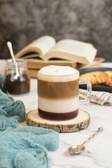 Obraz na płótnie Canvas A cup of layered mocchiato latte coffee topped with mousse foam on a table with cookies and book in background and copy space. The drink is based on the espresso and steamed milk combination