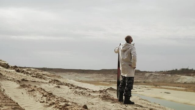 Handsome bald man posing with sandboard in desert or sand quarry