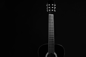 Acoustic black guitar resting against a black background with copy space