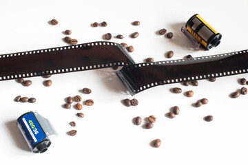 Una tira de película analógica de 35mm junto a granos de café y dos rollos de película...