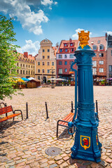 Traditional blue water pump with gryphon head crest from Szczecin city emblem and old town square in background. Gryphon is Stettin emblem since 1360