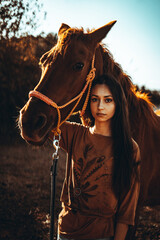 Fototapeta premium Chica joven andaluza ecuestre montando sobre caballo marron en un campo natural sin silla ni riendas en el sur de españa al atardecer feliz