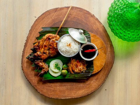 Top view of juicy Chicken Inato with a serving of garlic rice and atchara. Placed on a circular wooden tray. A popular grilled dish in Cebu.