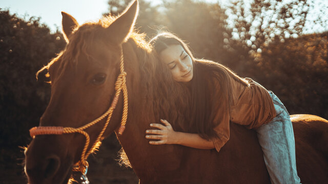 Chica joven andaluza ecuestre montando sobre caballo marron en un campo natural sin silla ni riendas en el sur de españa al atardecer feliz