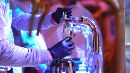 A man's hand in black protective gloves pours beer from a tap into a glass goblet. Steward shed A...