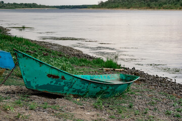 Old boats made of wood and metal on the river Bank among rocks and vegetation. Parked water transport in nature. Simple landscape.