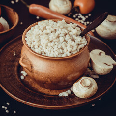 A small earthenware pot with pearl barley porridge on a brown ceramic dish. Russian kitchen. Selective focus. Tinted photo.
