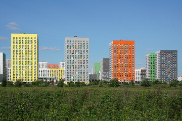  New houses of the city in a green field against a blue sky. The concept of the onset of the city on nature.