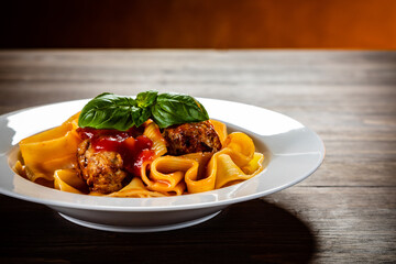 Pasta with meatballs in tomato sauce on wooden table against gradient orange background
