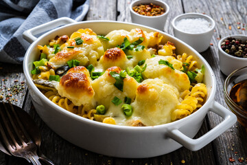 Noodle casserole with cauliflower, minced meat, mozzarella cheese and cream sauce on wooden table

