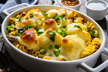 Noodle casserole with cauliflower, minced meat, mozzarella cheese and cream sauce on wooden table
