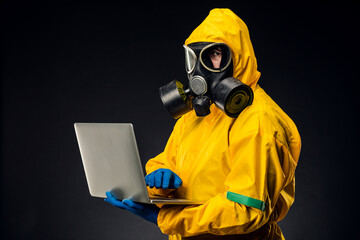 A man in a yellow protective chemical suit holds a laptop on a black background, a virologist uses a computer.