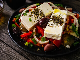 Fresh Greek salad - feta cheese, tomatoes, cucumber, red pepper, black olives and onion on wooden table
