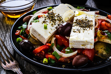 Fresh Greek salad - feta cheese, tomatoes, cucumber, red pepper, black olives and onion on wooden table
