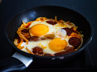 Breakfast - sunny side up eggs with sausages and onion in frying pan
