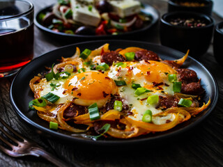 Continental breakfast - sunny side up eggs  on sausages, onion and greek salad on wooden table
