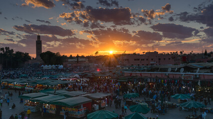 Yamaa el Fna Square with its markets and crowds of people and the tower of the mosque in the background, at sunset. Travel concept. Marrakech, Morocco