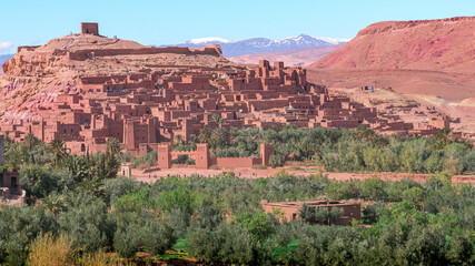 Daytime wide angle shot of Ksar de Ait Ben Haddou, with its abobe houses and towers, surrounded by palm trees and with the Atlas Mountains in the background, Morocco.